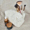 A Sherpa bag with a flower lining is pictured with various makeup brushes and face ointments - Fleece Chic