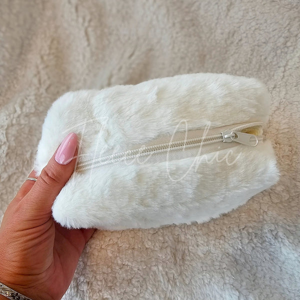 A small cosmetic fur bag that is white and is made with faux fur is displayed zipped closed - Fleece Chic