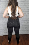 The rear view of a pair of opaque fleece lined tights that are black and stirrup style are shown paired with a white crop top - Fleece Chic