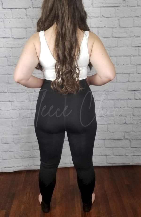 The rear view of a pair of opaque fleece lined tights that are black and stirrup style are shown paired with a white crop top - Fleece Chic