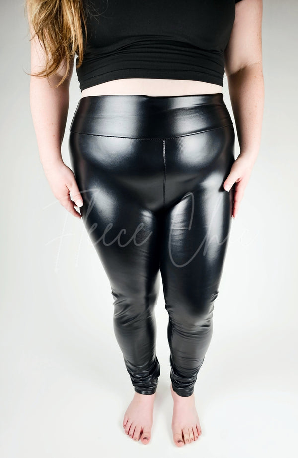 A plus size woman wears a pair of Vegan Leather Leggings by Fleece Chic paired with a black t-shirt.
