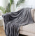 A gray plush blanket made of fleece is draped over an off white sofa - Fleece Chic