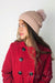 A woman wears a pink fleece beanie with a cute pom pom on it by Fleece Chic paired with a red coat.