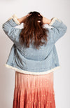 A woman stands facing away from the camera while showing off the backside of Fleece Chic's oversized fur lined trucker jacket.