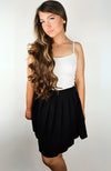 A woman wearing a black twirl skirt with a white thermal tank poses in front of a blank background - Fleece Chic