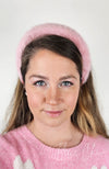A woman in a pink sweater wears a fur headband by Fleece Chic.