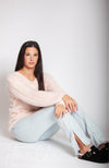 A woman sits on the floor while wearing a light pink fuzzy sweater, jeans, and black winter clogs - Fleece Chic