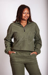 A woman has her hands in her pockets while looking at the camera wearing an army green sweat set by Fleece Chic.