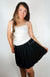 A woman wearing a black twirl skirt with a white thermal tank poses in front of a blank background - Fleece Chic.