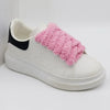 Unique shoelaces that are pink and fluffy are shown threaded through the loops of a pair of white sneakers with a black back - Fleece Chic