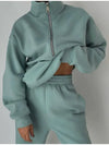 A teal gray sweatsuit with matching sweatshirt and sweatpants are worn by a woman who is holding up the top to expose her midriff  - Fleece Chic