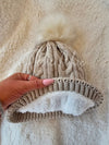 A beige Fleece Hat by Fleece Chic has its cozy sherpa interior displayed.