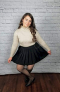 A high waist pleated skirt that is black is worn by a woman who is curtsying in cozy tights and heels - Fleece Chic