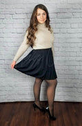 A black high waist pleated skirt is worn by a girl in black opaque tights and a sweater - Fleece Chic