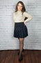 A black high waist pleated skirt is worn by a girl in black opaque tights and a sweater - Fleece Chic