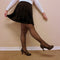 A high waist pleated skirt that is black is worn by a woman in faux translucent fleece tights and heels making a funny pose - Fleece Chic