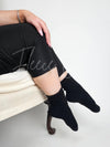 A woman poses in a black pair of boot socks while sitting down - Fleece Chic