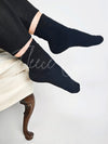 A woman poses in a black pair of boot socks while sitting down - Fleece Chic